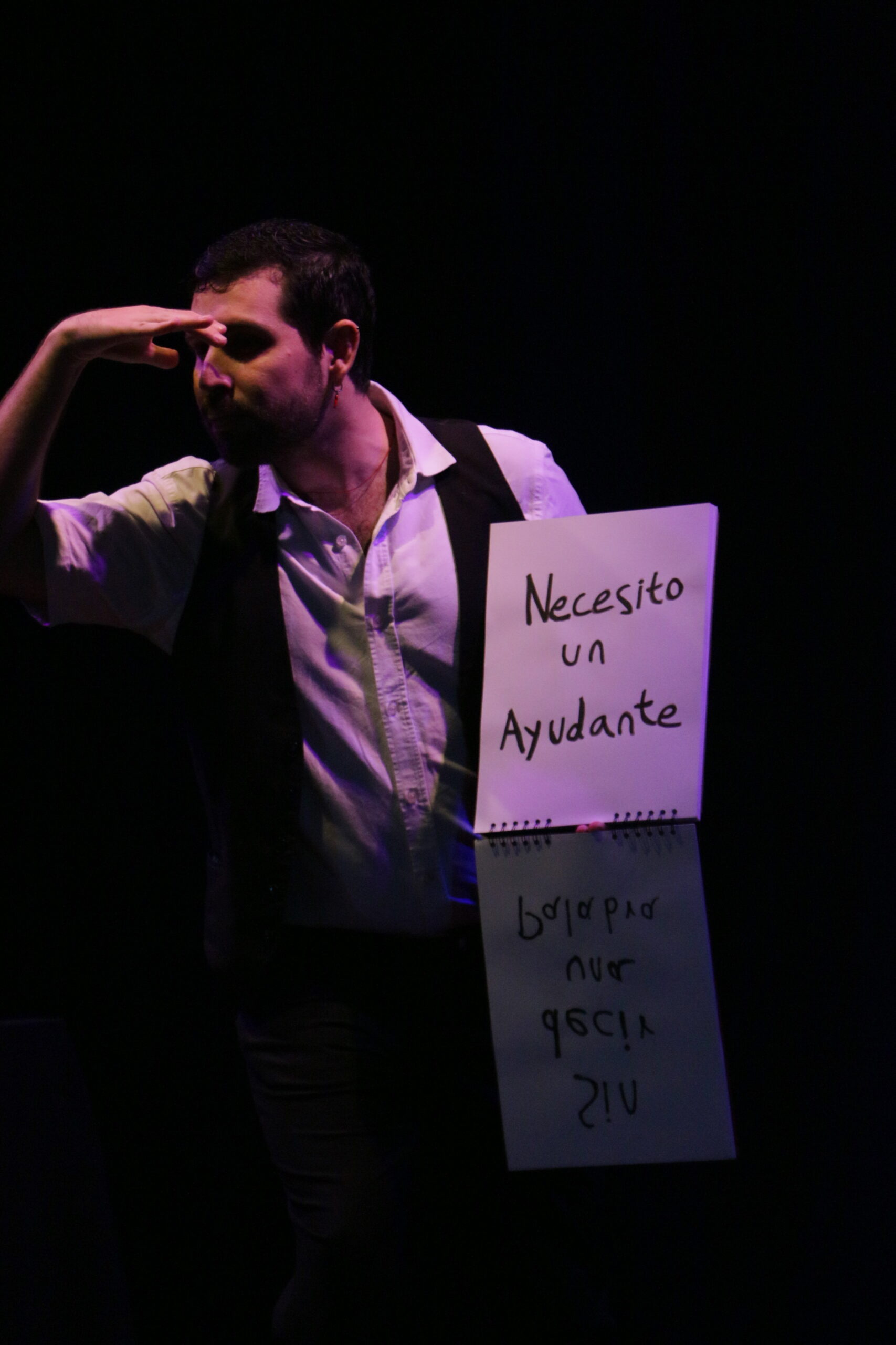 Artista de El Colectivo Mágico en escena sosteniendo un cartel que dice "Necesito un ayudante"