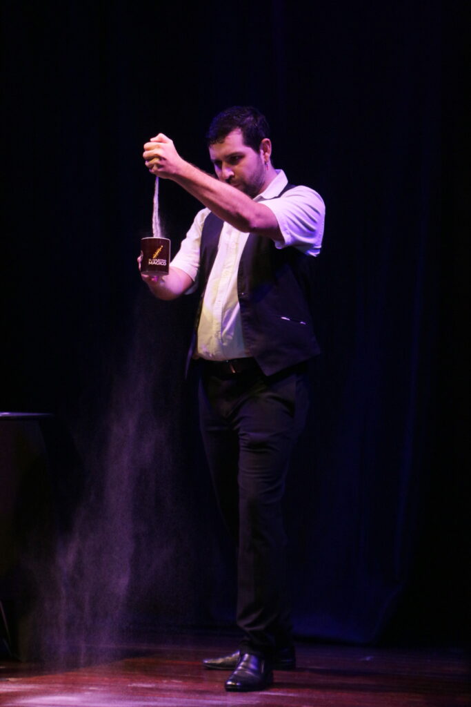 Un mago dejando caer arena de su mano, hacia un vaso